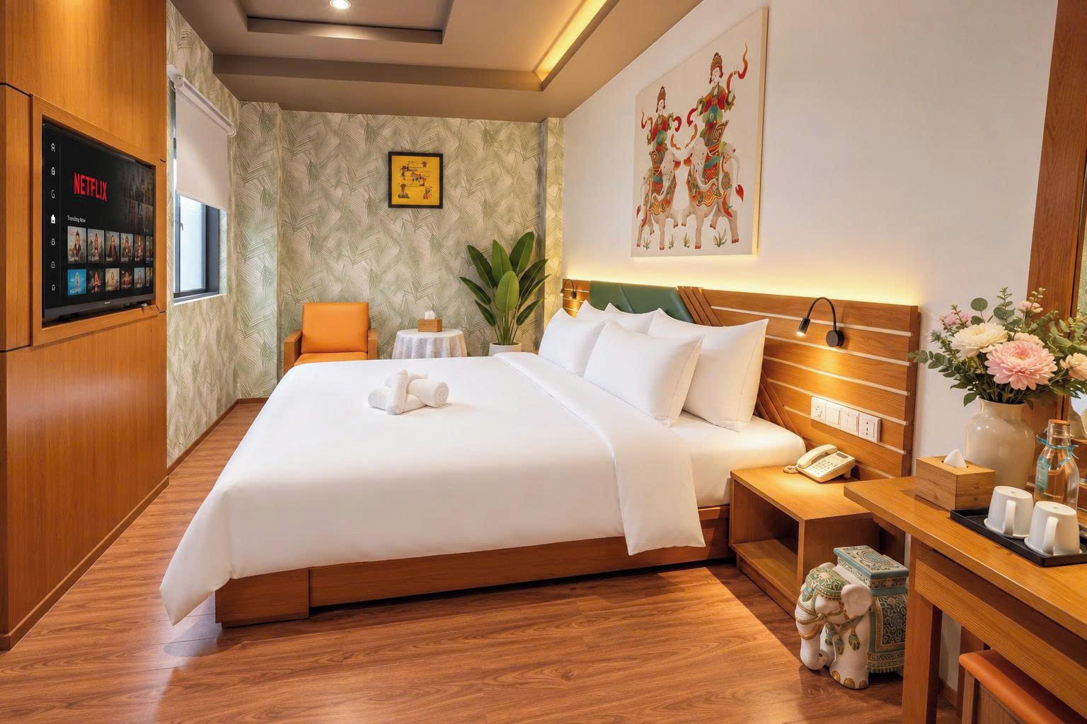 A hotel room with a large bed, a bedside table with a phone, a small table with a plant, and a wall-mounted TV displaying Netflix.