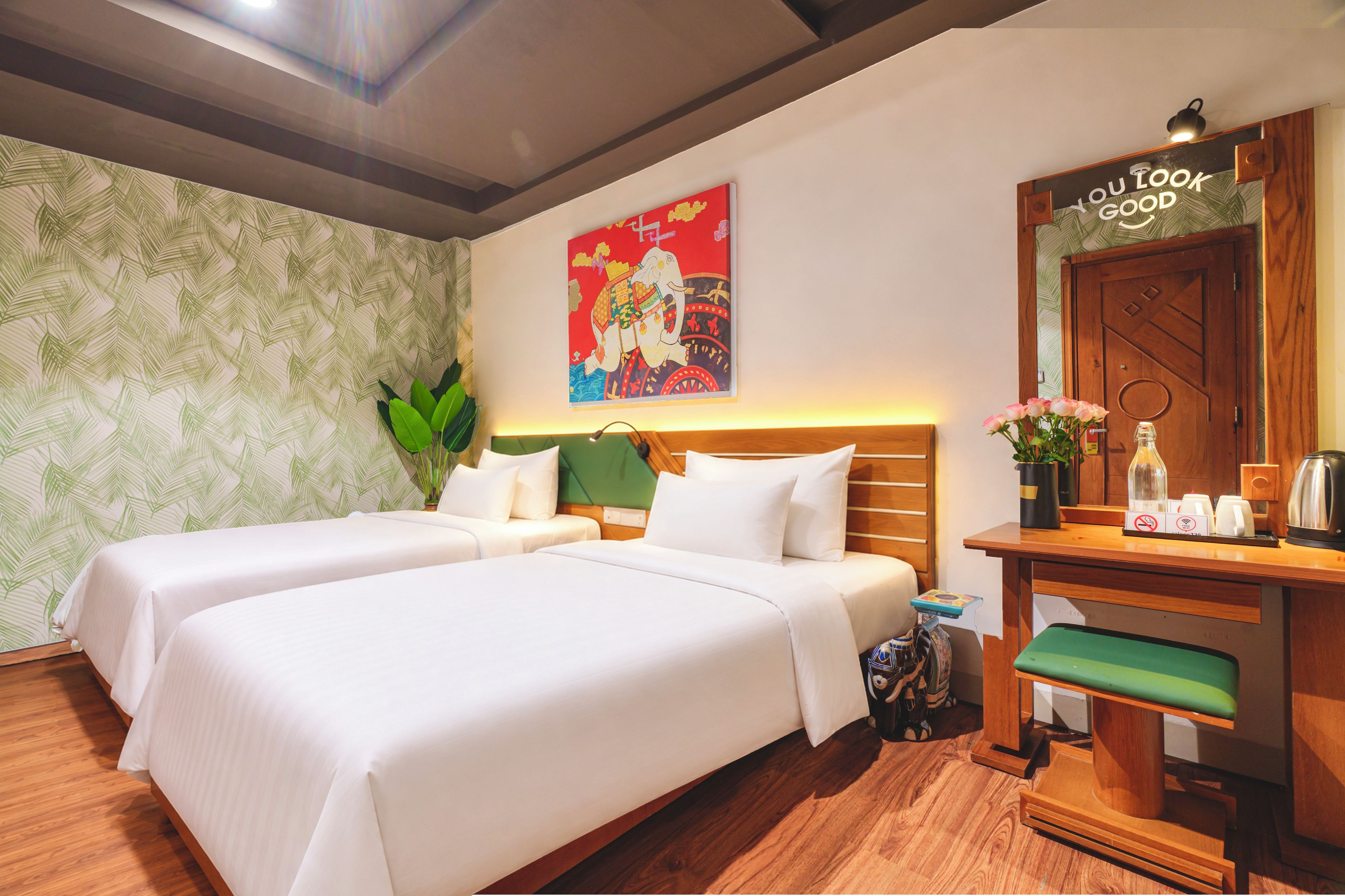 Habitación de hotel con dos camas, cabecero de madera, un cartel en la pared, un espejo y una mesita con artículos de aseo.