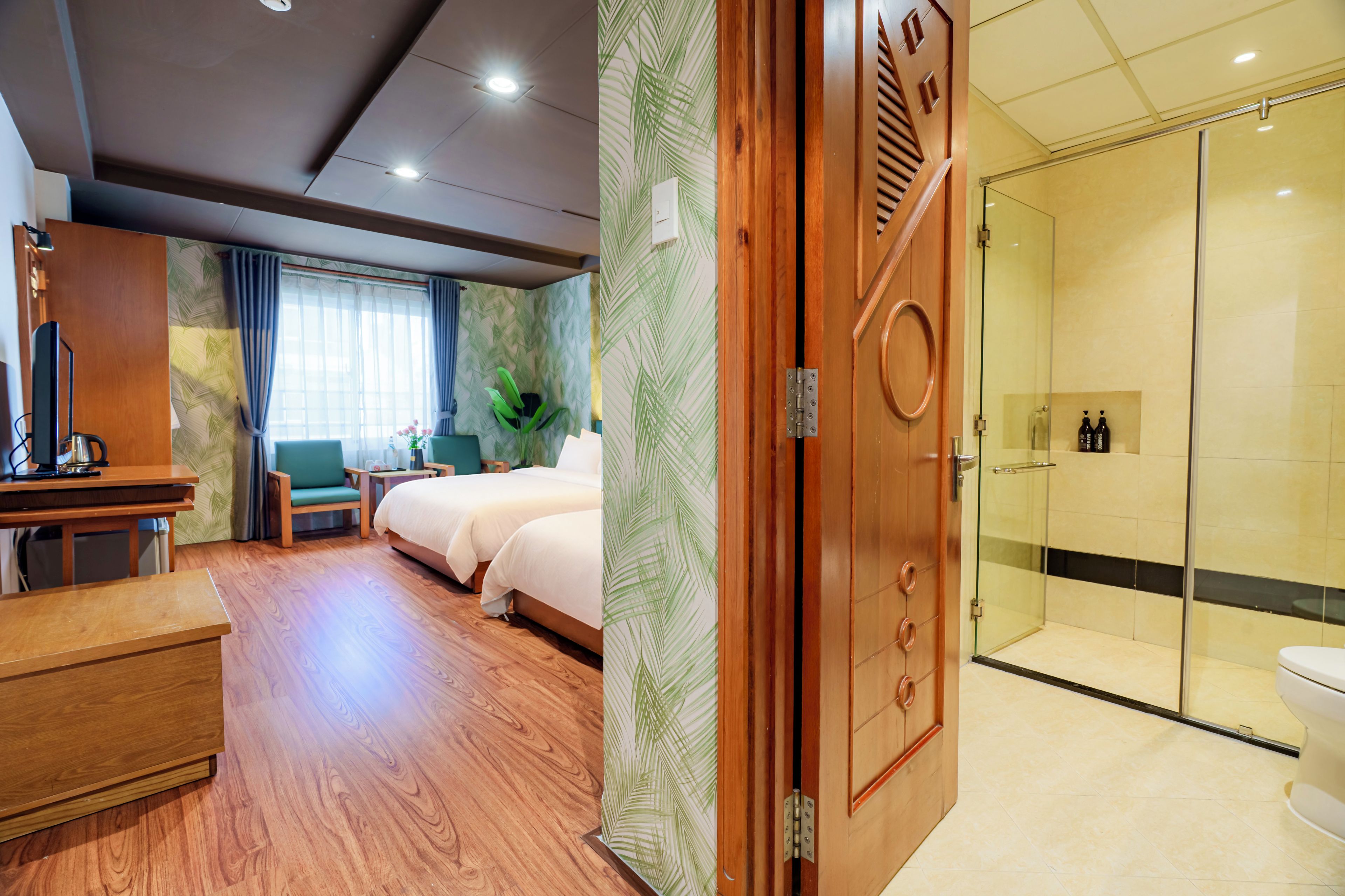 Een hotelkamer met een bed, nachtkastje en bureau met stoel. Er is een douchecel met een glazen deur en een toilet.