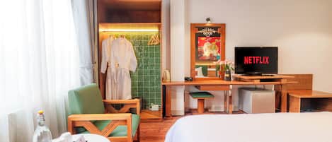 A hotel room with a bed, a desk with a television, a chair, a table with a bottle and glasses, and a shower area with towels.