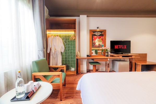 Una habitación de hotel con una cama, un escritorio con televisor, una silla, una mesa con una botella y vasos, y una zona de ducha con toallas.