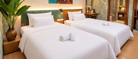 Una habitación de hotel con dos camas, una planta grande, un cuadro y un espejo.