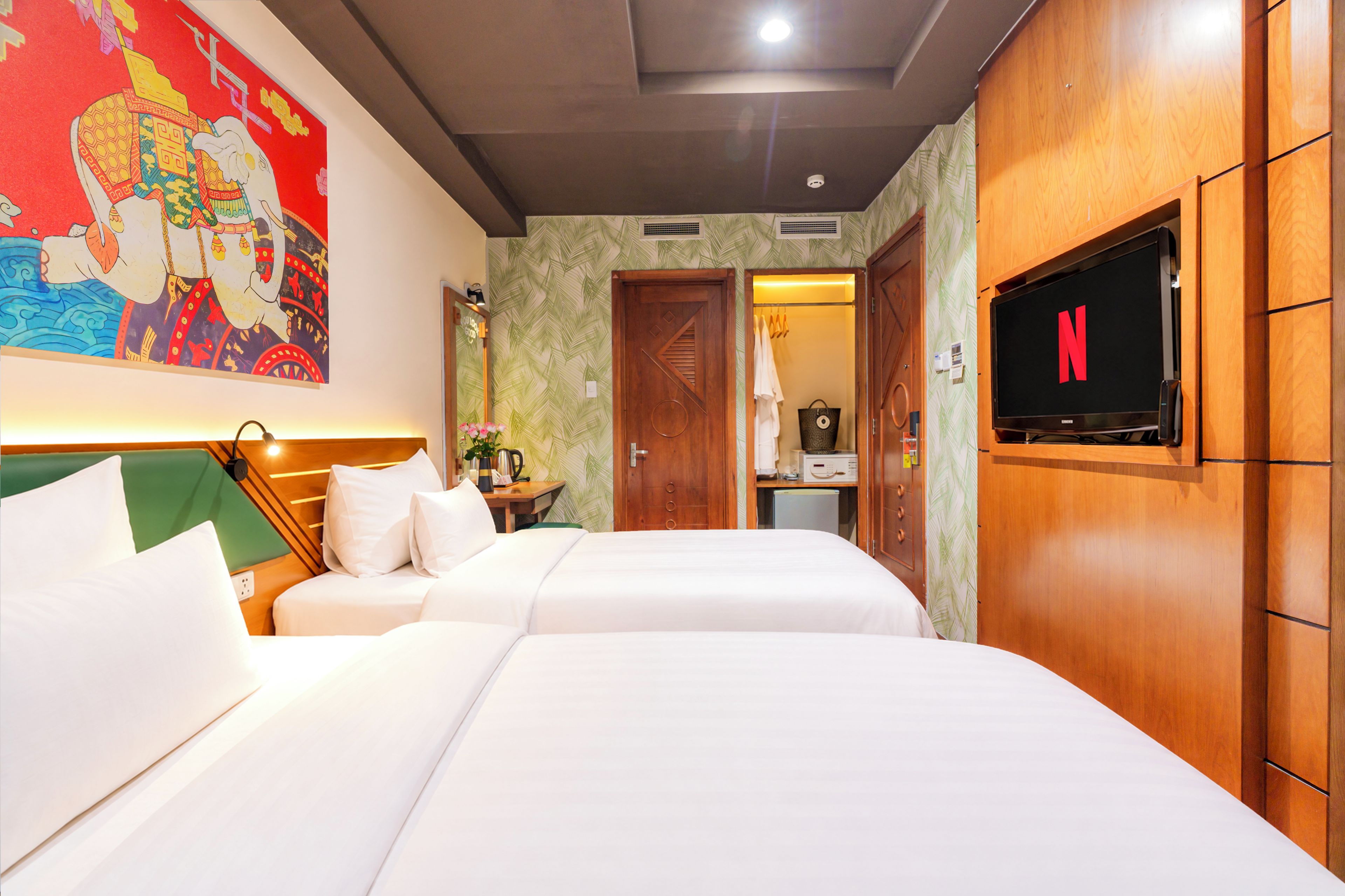 A hotel room with two beds, a television, a painting, and a wardrobe.