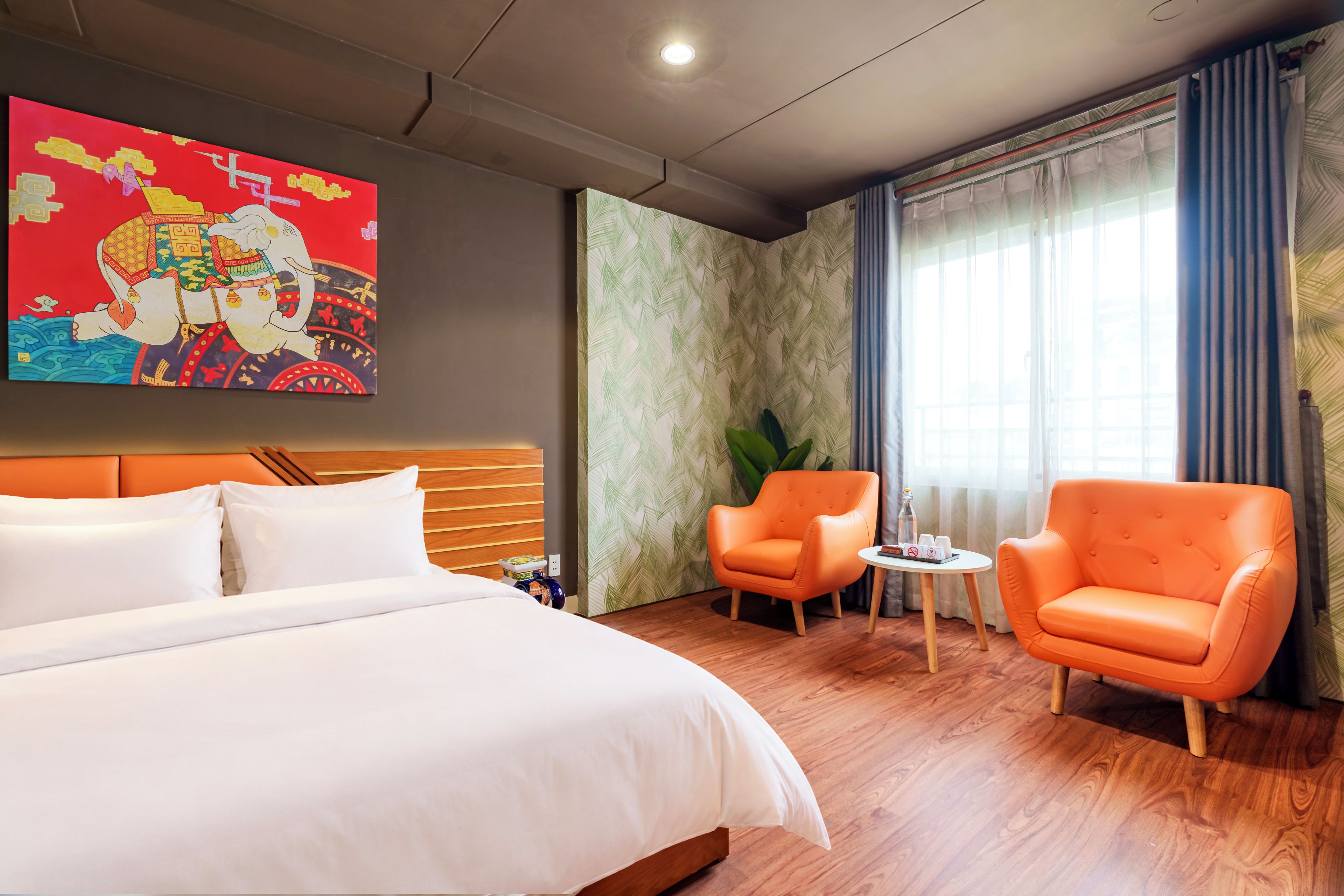 Een hotelkamer met een groot bed, twee fauteuils, een bijzettafeltje en een decoratief wandobject.