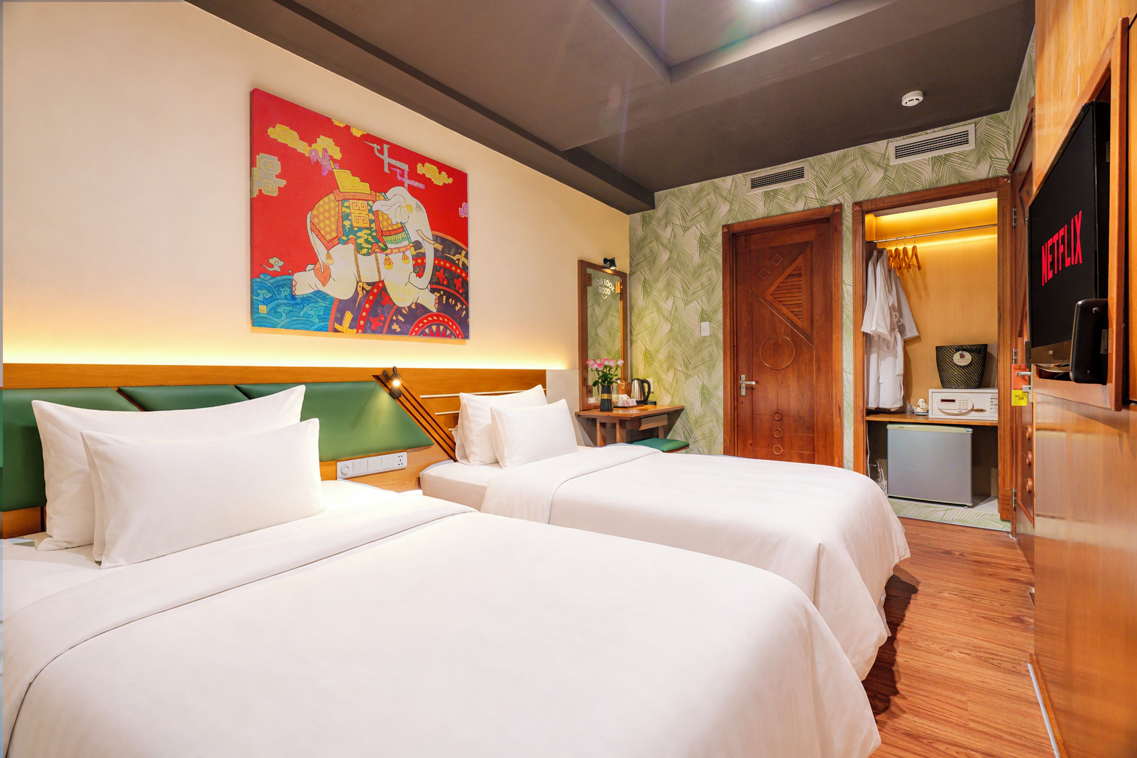 Habitación de hotel con dos camas, un cuadro en la pared, una mesita con una planta y una puerta que da a un baño con ducha.