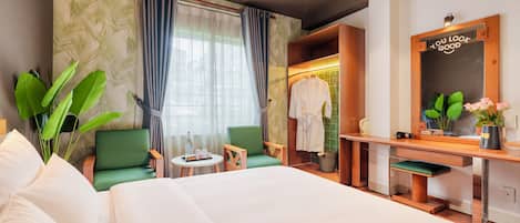Habitación de hotel con una cama, dos sillas, una mesita, un tocador con espejo y vistas al exterior por una ventana.