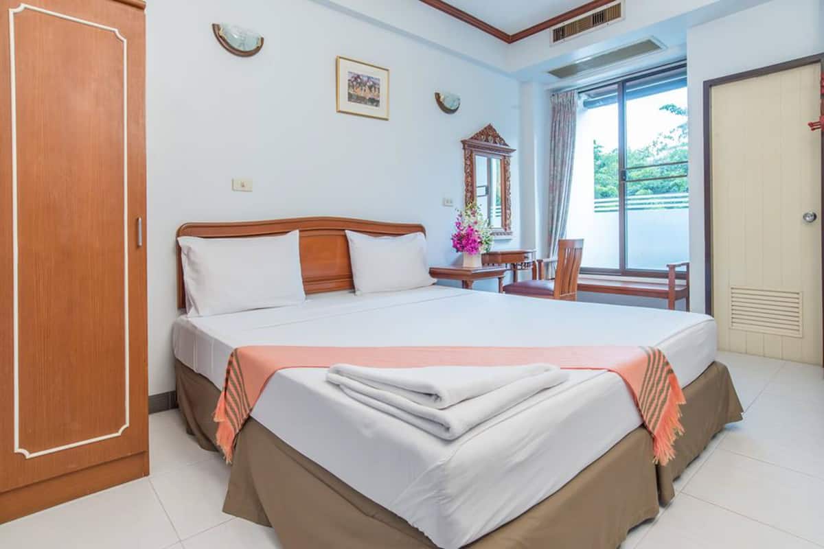 A hotel room with a large bed, wooden headboard, a desk with a chair, a window with curtains, and a door.