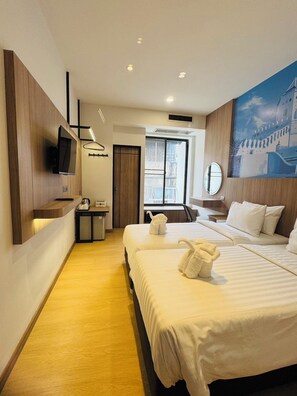 A hotel room with two beds, a TV mounted on the wall, a small desk with a kettle, and a large window with a view of buildings. - New Siam II (Bangkok)