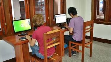 Two individuals seated at wooden desks with computers, in a room with wooden paneling and a carpeted floor.