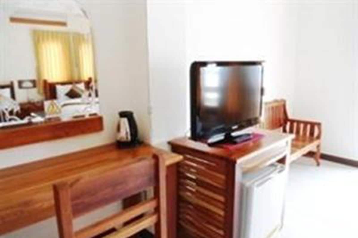A hotel room with a wooden desk, a television, a chair, and a small kitchenette area.