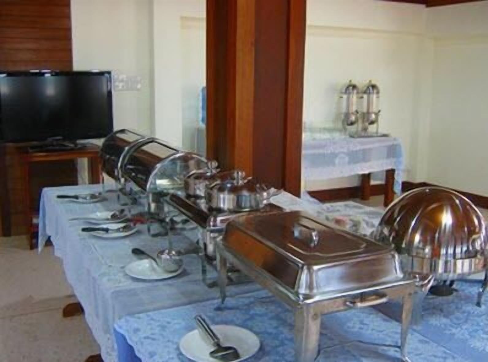 Montaje de bufé con varios recipientes de comida y utensilios sobre una mesa, un televisor al fondo y un pilar de madera.