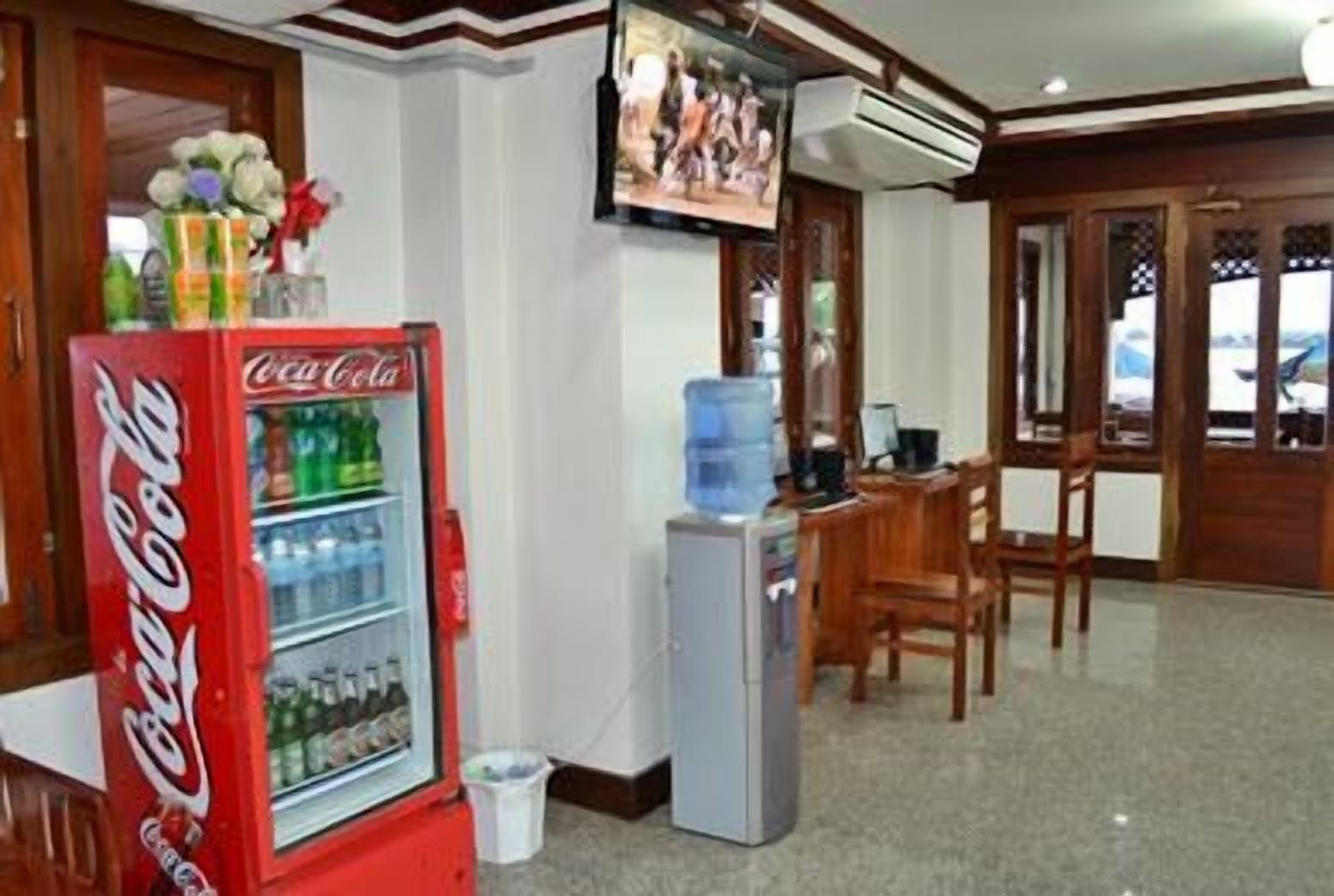 A room with a Coca-Cola refrigerator, a water dispenser, a television, and wooden furniture.