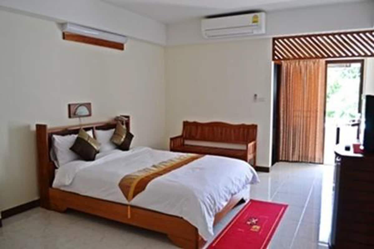 A hotel room with a wooden bed, a red carpet, and a view of the outdoors through a window with curtains.