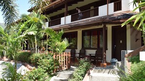 A two-story building with a balcony, surrounded by lush greenery and a stone pathway.