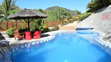 Relax by the serene pool surrounded by lush greenery and palm trees.