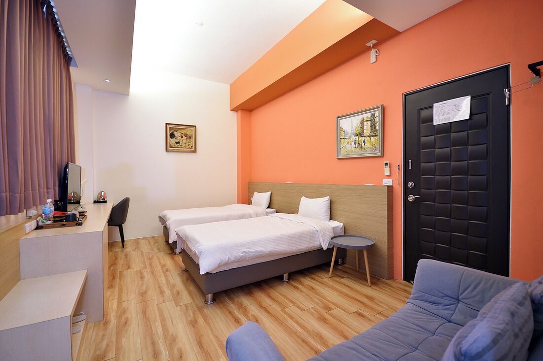 A hotel room with two beds, a desk, a chair, a small table, and a door with a notice.