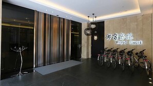 Una entrada de hotel moderna con fachada de vidrio, zona de estacionamiento para bicicletas y un cartel que indica que es el Royal Hotel.
