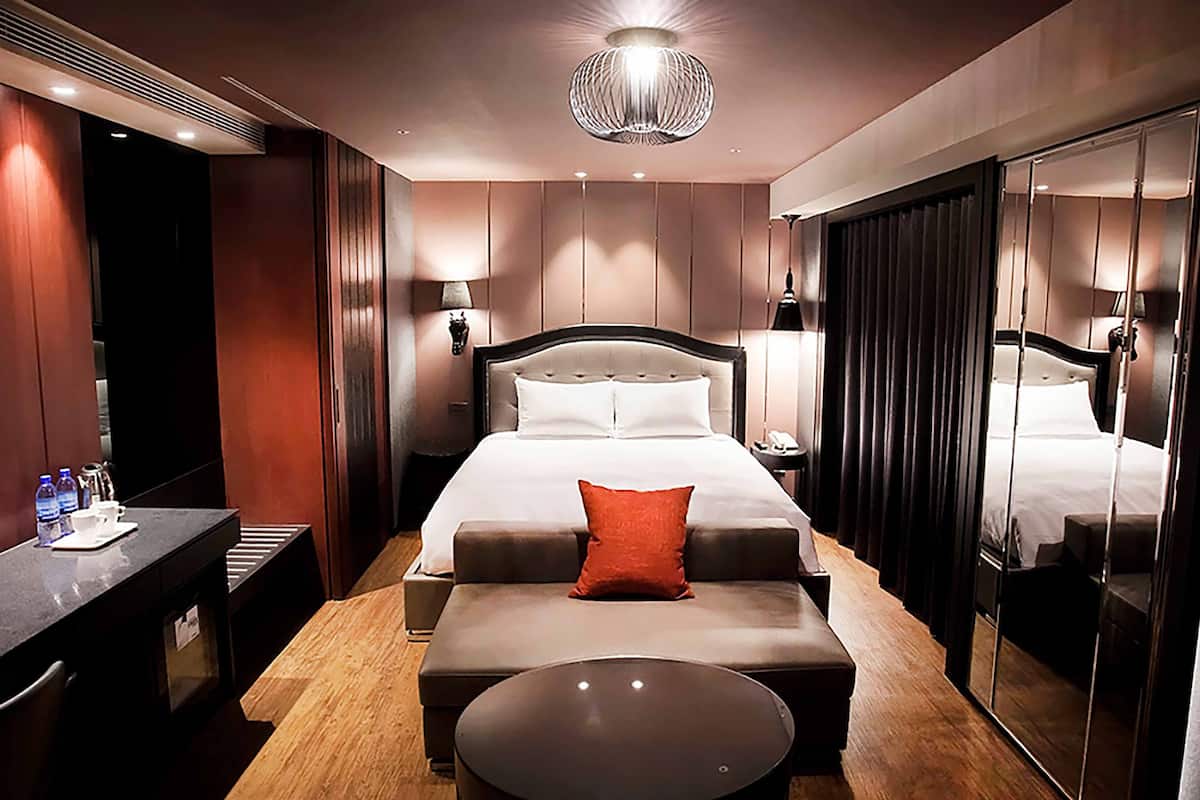 Ein modernes Hotelzimmer mit einem großen Bett, einem Nachttisch mit Lampe, einem kleinen runden Tisch und einem Spiegel.