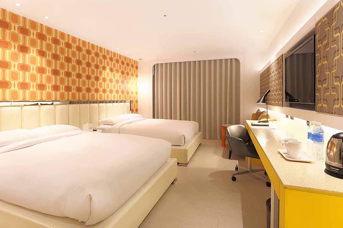 Ein Hotelzimmer mit zwei Betten, einem Schreibtisch, einem Stuhl, einem Fernseher und einer Wand mit Muster.