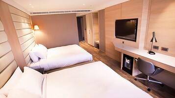 A hotel room with two beds, a desk, a chair, a TV, and a lamp.