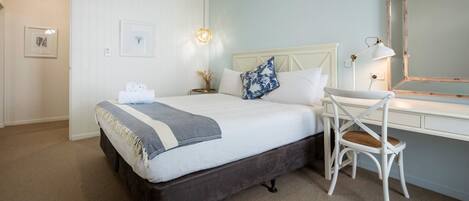 A bedroom with a bed, a desk, a chair, a mirror, and wall-mounted air conditioning.