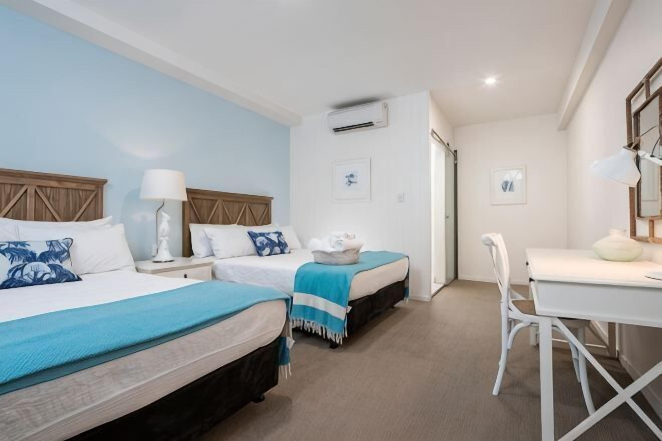 A hotel room with two beds, a desk, a chair, and a small table.