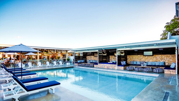 A pool area with lounge chairs and a stone wall seating area. - Rambutan Resort (Townsville)
