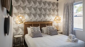 A neatly arranged bedroom with a large bed, two bedside tables, a headboard, and a window with curtains. - Rambutan Resort (Townsville)