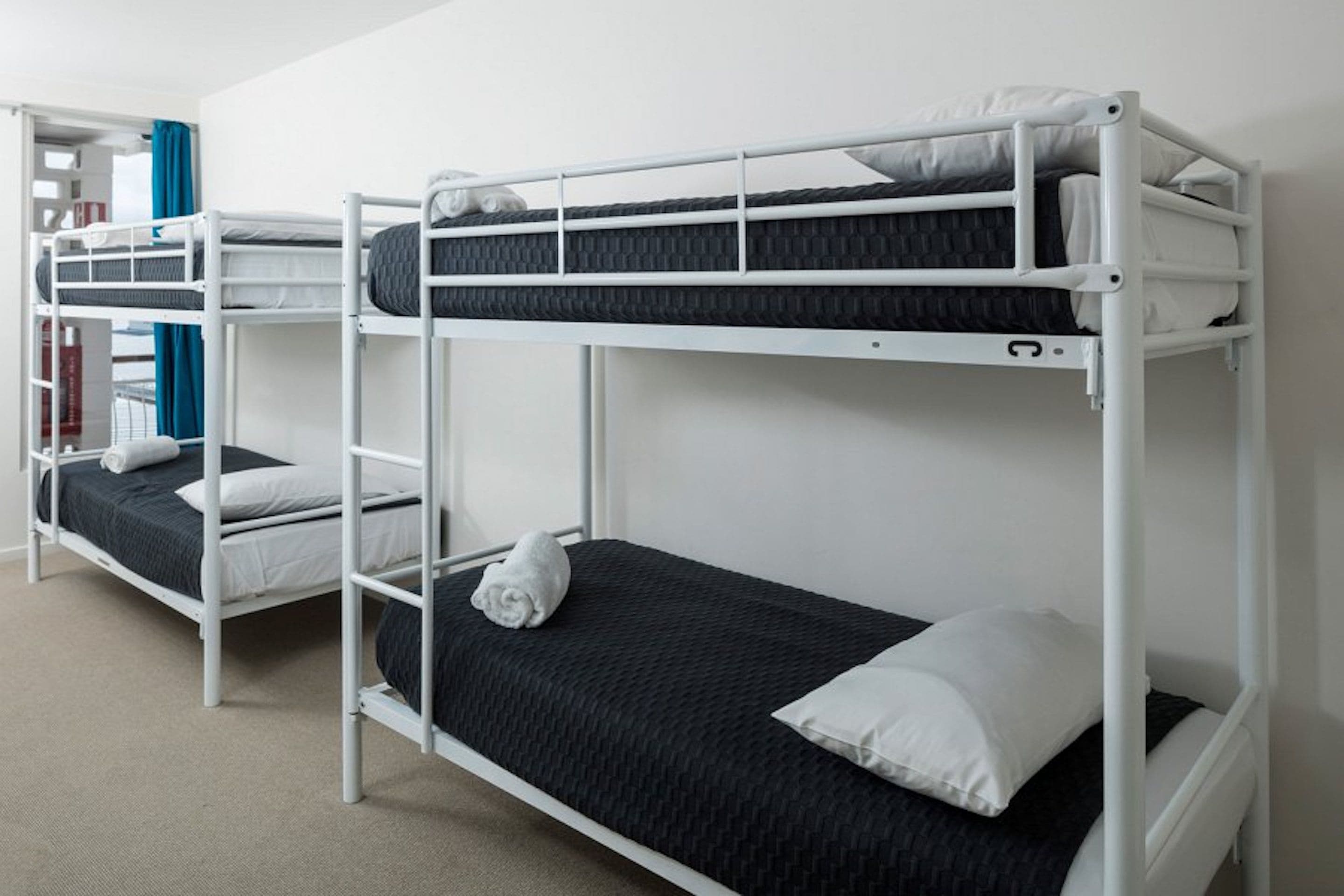 A bunk bed room with white metal frames, black bedding, and a blue curtain.