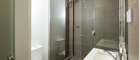 Un baño moderno con ducha de vidrio, inodoro blanco y lavamanos con espejo.