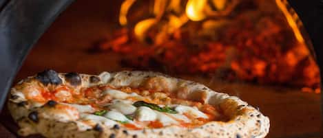 A pizza in a wood-fired oven with visible flames.
