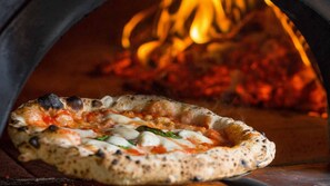 A pizza in a wood-fired oven with visible flames.
