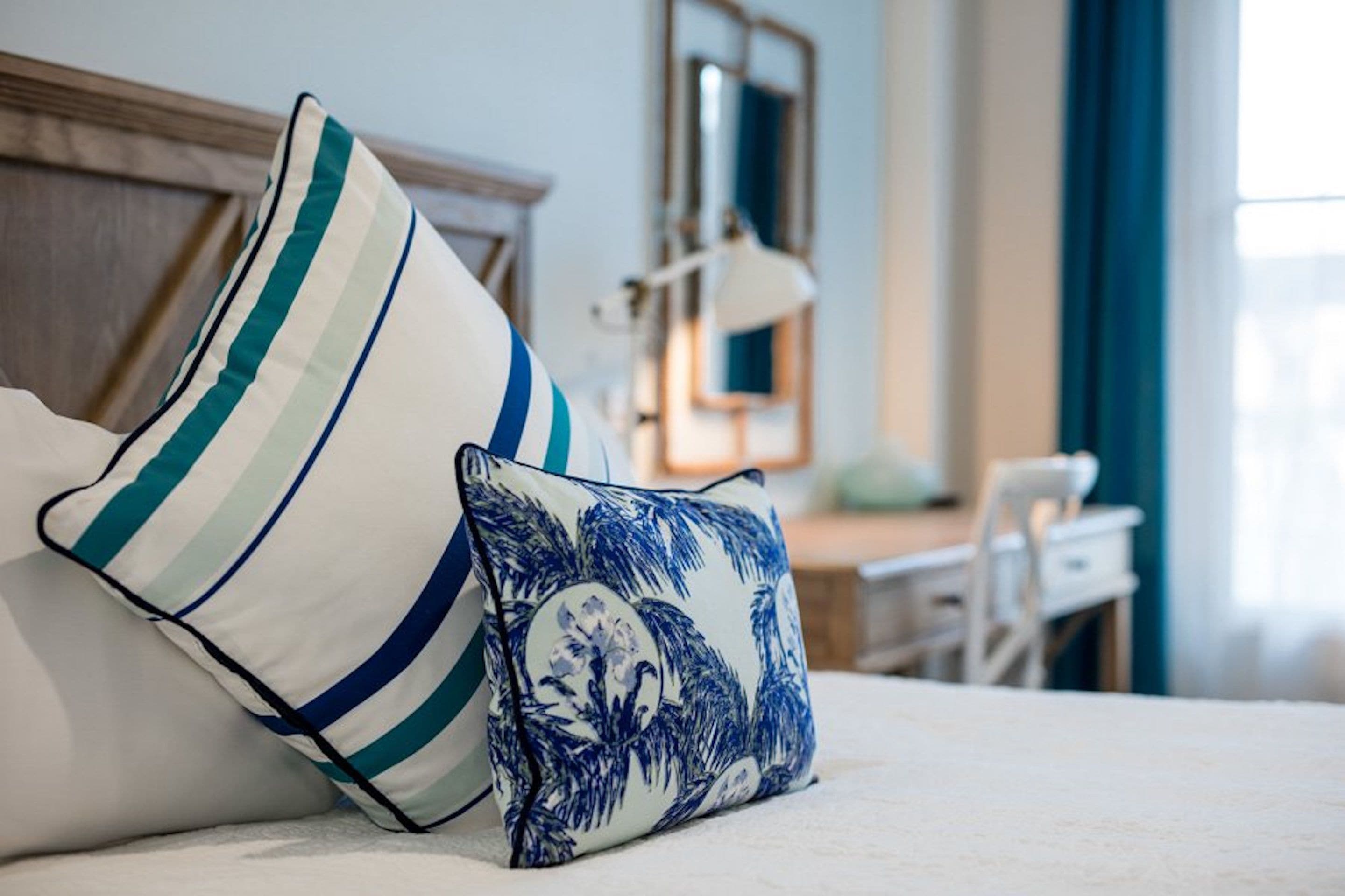 Un lit avec deux oreillers, l’un à rayures et l’autre avec un motif floral bleu, dans une pièce dotée d’une tête de lit en bois, d’un bureau et d’une chaise.
