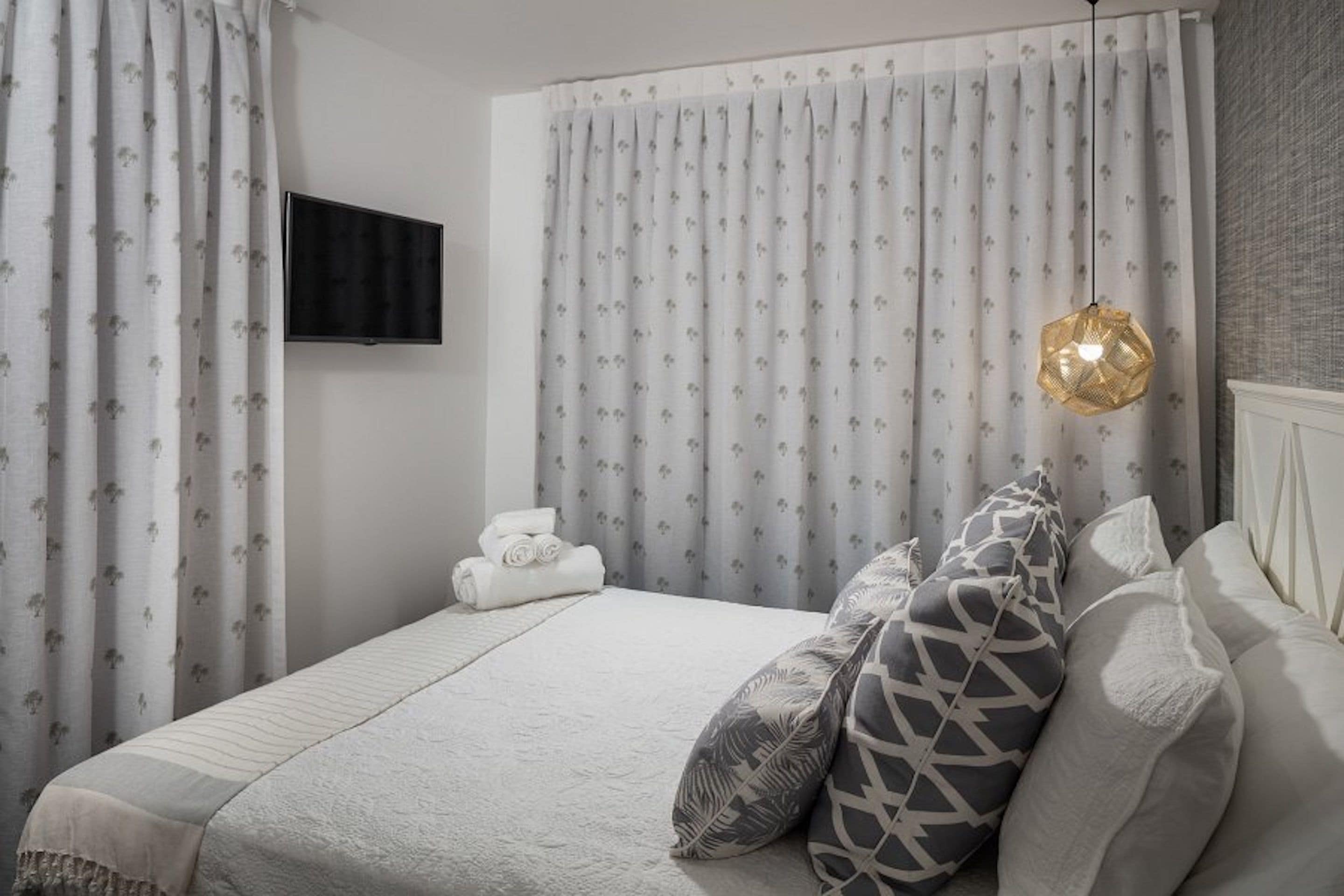 A bedroom with a bed, pillows, a TV, and curtains.
