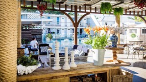 An outdoor seating area with wicker furniture, potted plants, and a view of a pool and buildings in the background. - Rambutan Resort (Townsville)