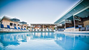 A pool area with lounge chairs and umbrellas, a covered seating area, and a stone building.