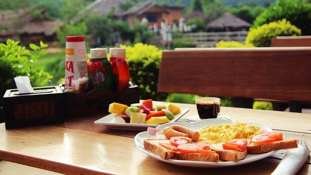 Una mesa de desayuno con tostadas, huevos y fruta, una taza de café y condimentos.
