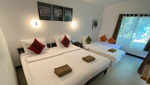 Habitación de hotel con dos camas, cada una con sábanas blancas y almohadas en rojo, verde y naranja. Cuenta con luces empotradas en la pared, una ventana con cortinas y una mesita.