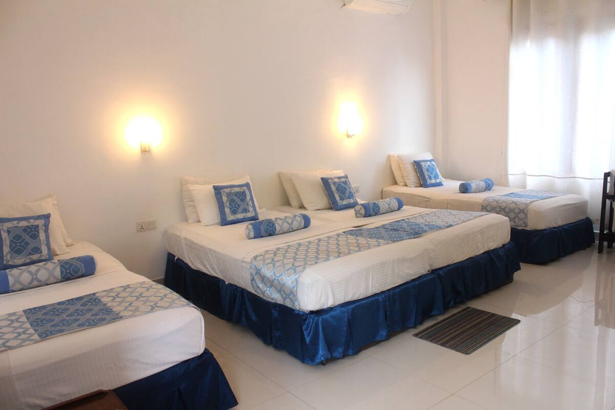 A hotel room with four beds, each with blue and white bedding, and two wall-mounted lights.