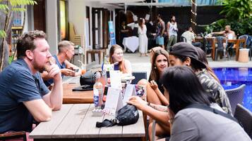A group of people seated at an outdoor table with a menu, surrounded by a pool and greenery.
