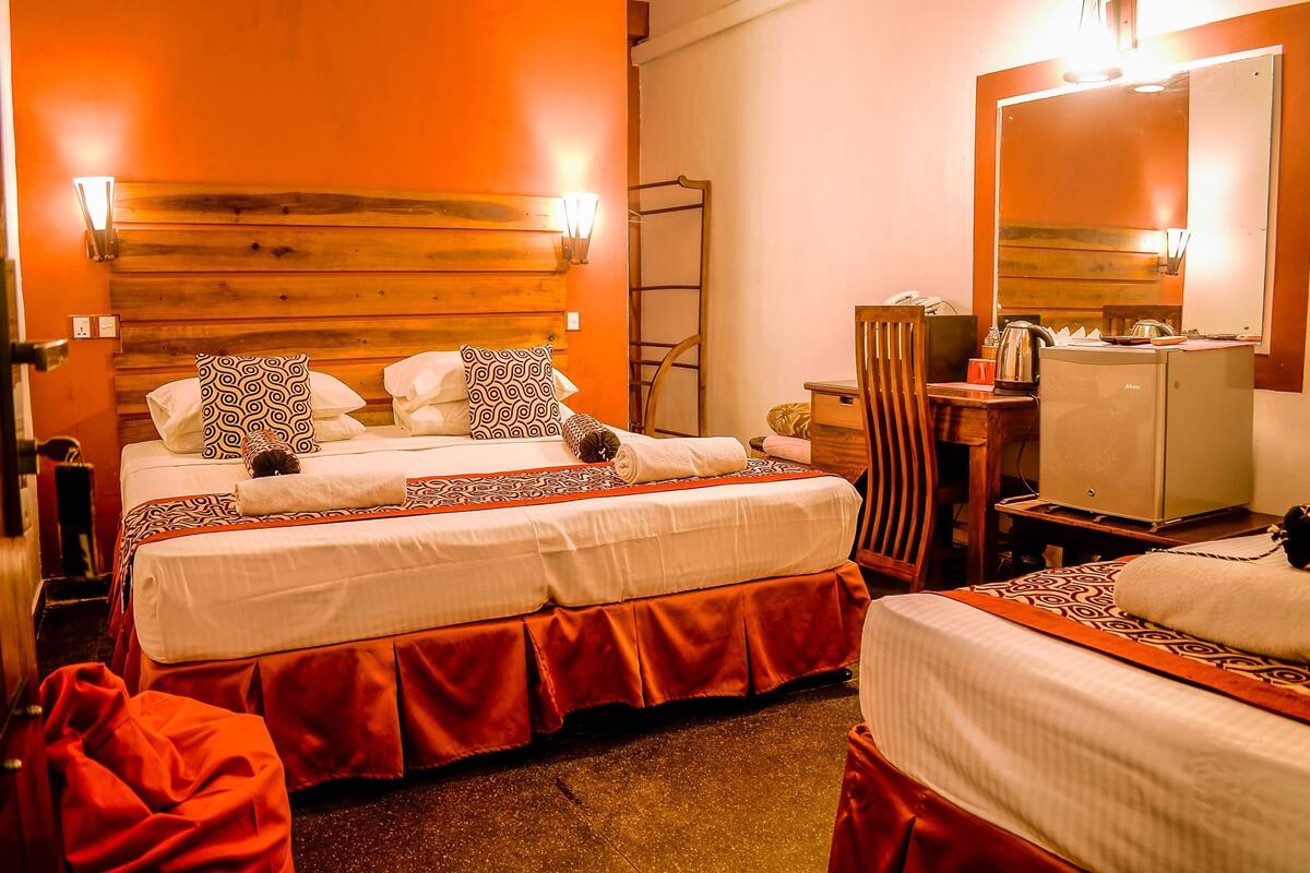 A hotel room with two beds, a wooden headboard, a mirror, a desk with a lamp, and a minibar.