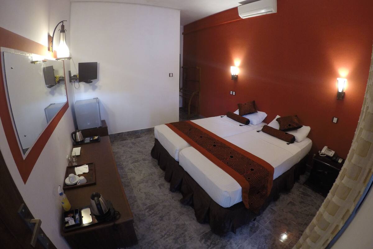 A hotel room with a bed, bedside tables, a desk, a mirror, and a ceiling fan.