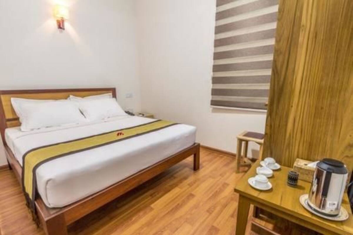 Ein Hotelzimmer mit einem hölzernen Bett, einem Nachttisch mit Kaffeemaschine und einem Fenster mit gestreiften Jalousien.
