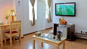 Ett hotellrum med ett skrivbord i trä, en stol, en tv som är monterad på väggen, en kaffebryggare och en korg med frukt.