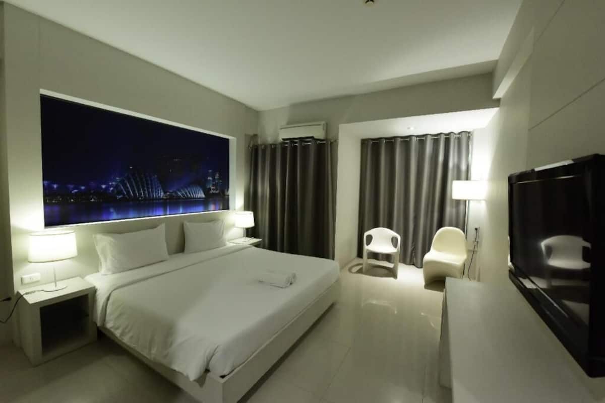 Une chambre d’hôtel avec un grand lit, une télévision, un bureau et une vue sur le paysage urbain illuminé la nuit.