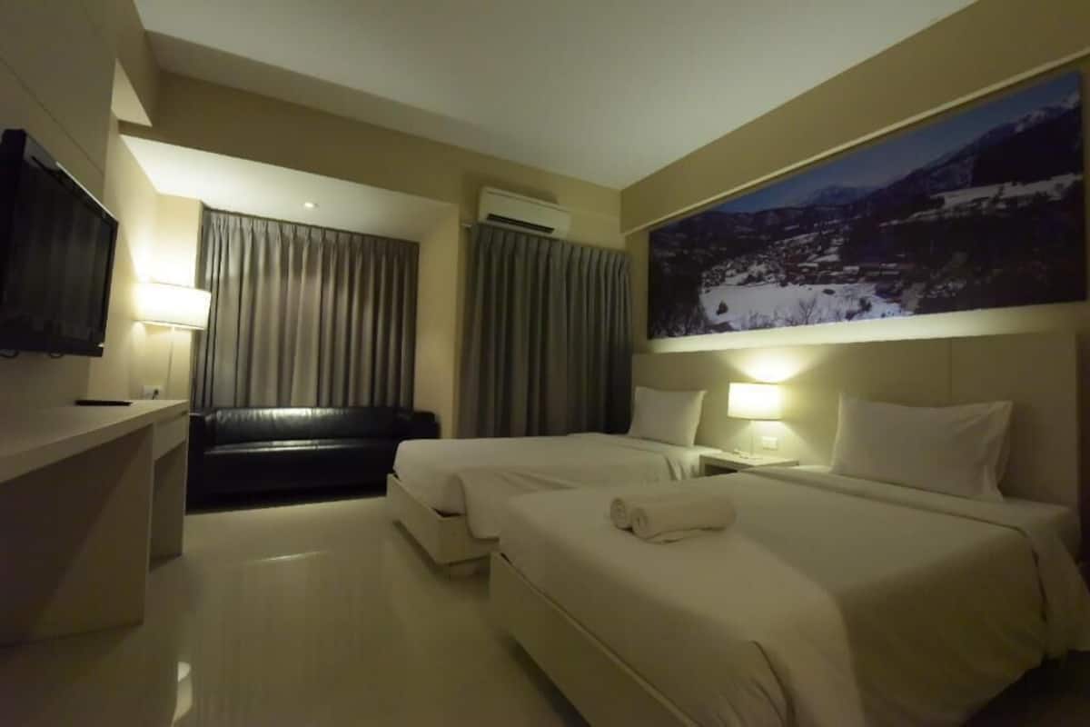 Une chambre d’hôtel avec deux lits, un téléviseur à écran plat, un bureau et un tableau représentant un paysage enneigé.