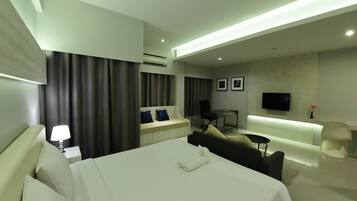A modern hotel room with a large bed, a sofa, a desk, and a TV.