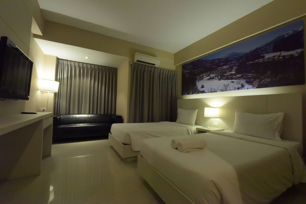 Habitación de hotel con dos camas, televisión, escritorio y un cuadro en la pared.