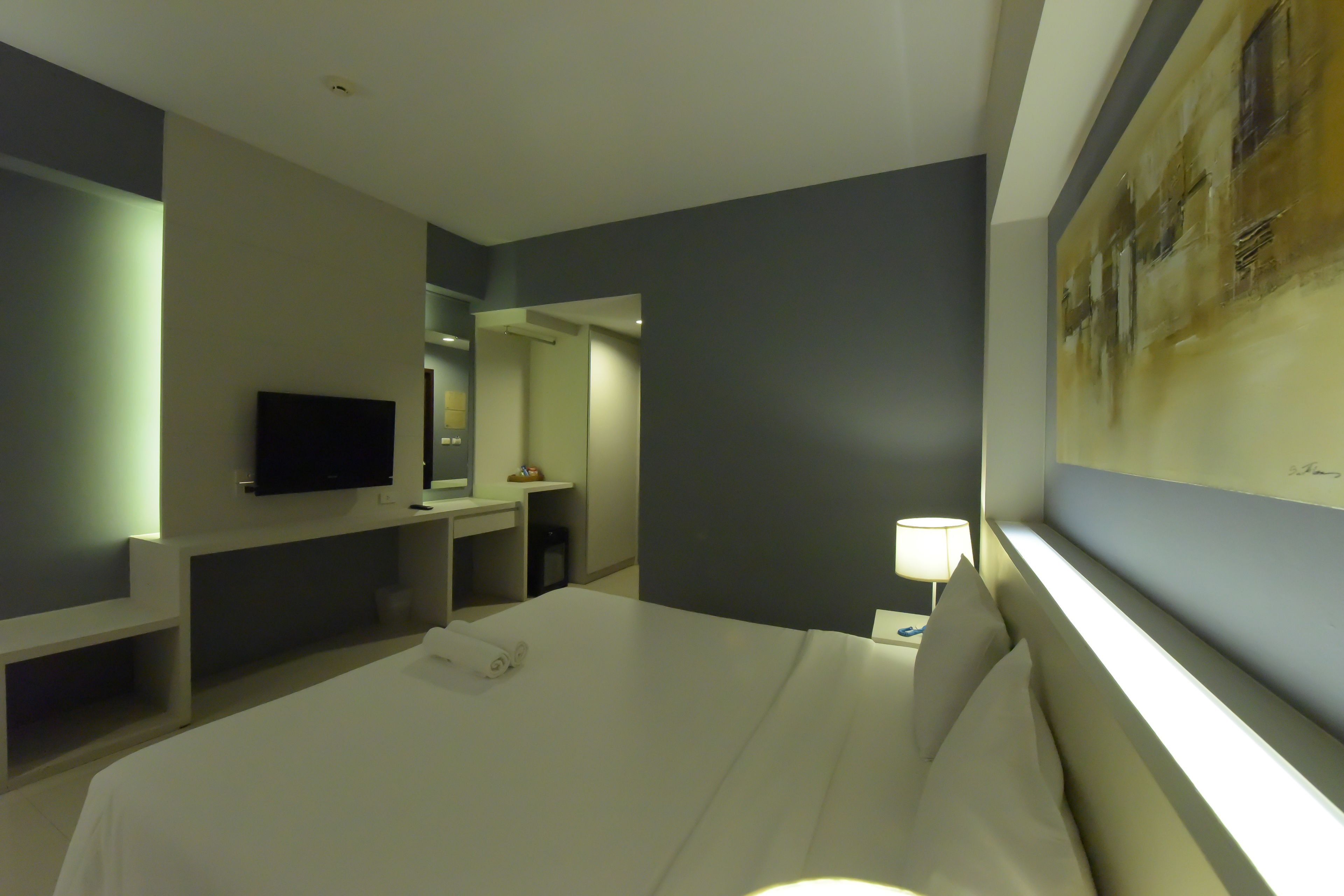 A hotel room with a bed, a TV, a desk, and a painting on the wall.