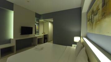 A hotel room with a bed, a TV, a desk, and a painting on the wall.